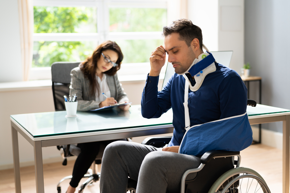 Man in wheel chair with arm in sling and neck brace on discussing his case with a New York Workers' Compensation lawyer