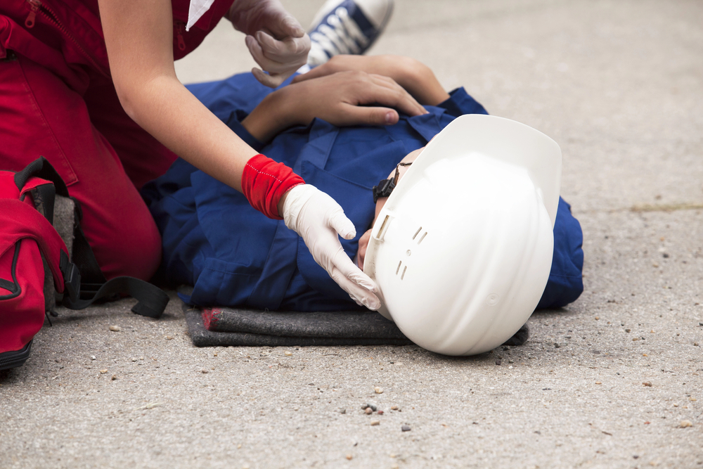 Man laying on ground as coworker checks on him before calling a New York Workers' Compensation lawyer for help